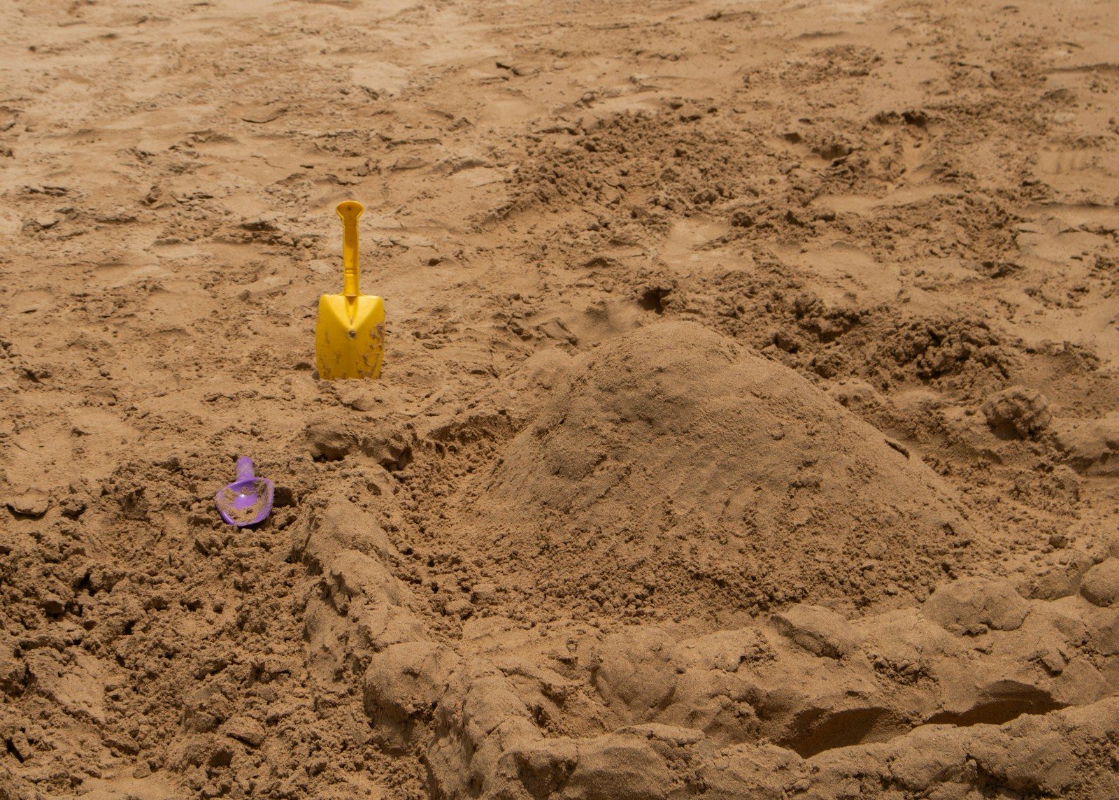 A yellow shovel and purple pail near a sandcastle symbolizing the parable of the talents.